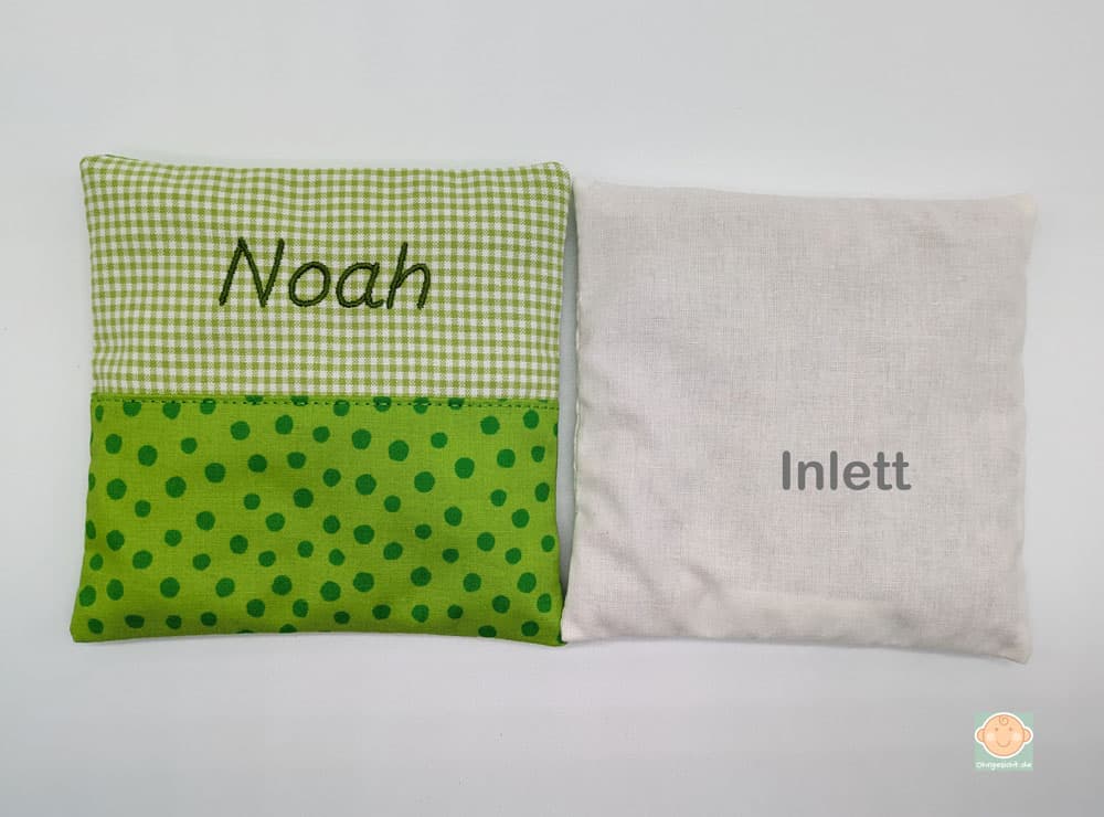 Grünes Kirschkernkissen mit Name und weißes Inlett.